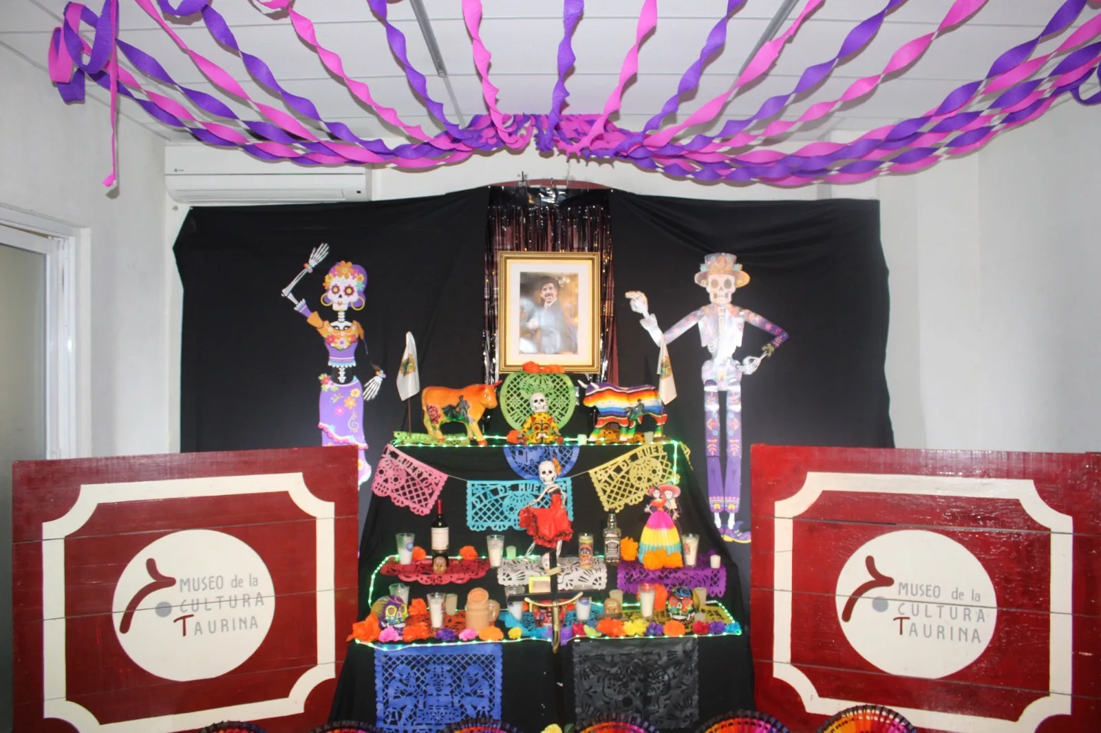 Altar de Día de Muertos en el Museo de la Cultura Taurina, con papel picado morado y figuras de catrines