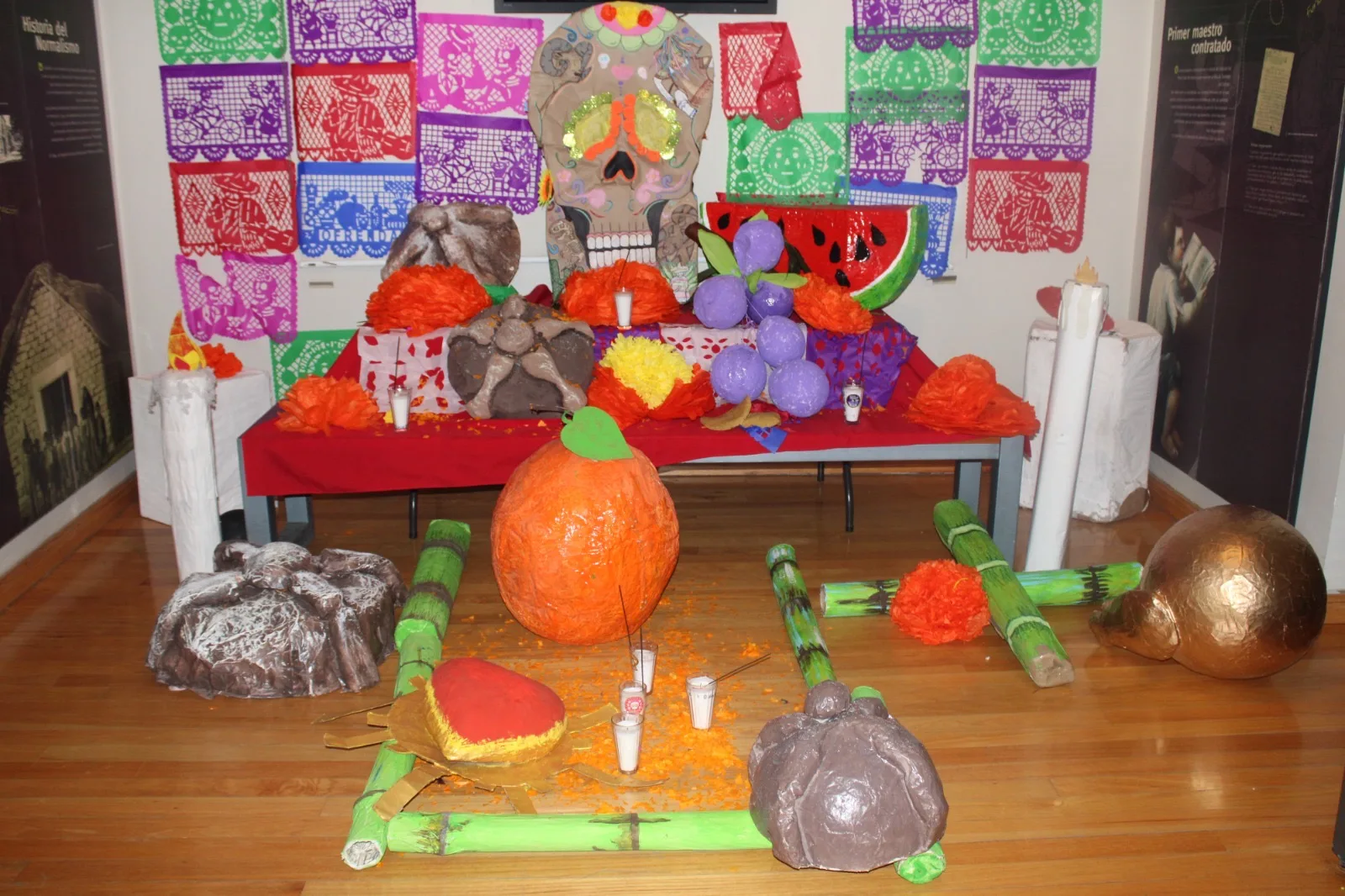 Altar de Día de Muertos con frutas de papel maché, calabazas y papel picado de colores