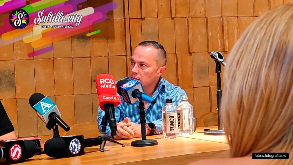 Hombre de camisa a cuadros azul frente a micrófonos de medios en la rueda de prensa del concierto de Ricardo Arjona en Saltillo