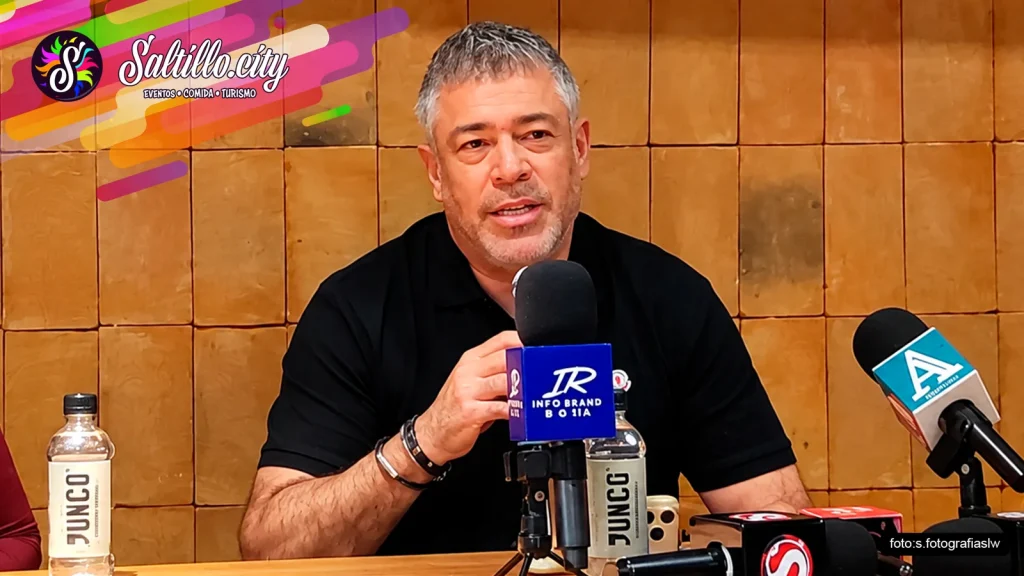 Hombre de playera negra habla ante micrófonos de medios en la rueda de prensa del concierto de Ricardo Arjona en Saltillo